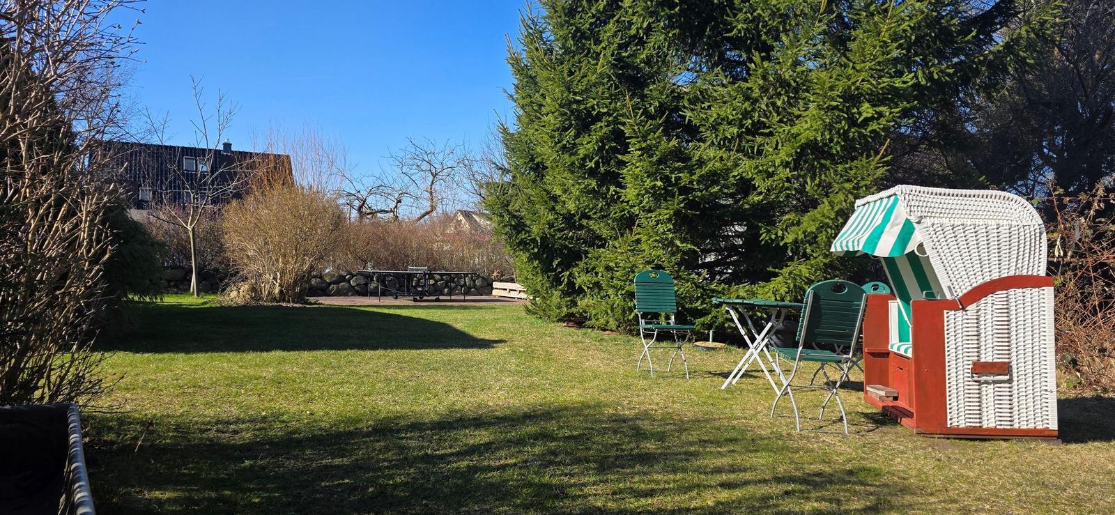 Garten mit Strandkorb, Tisch und Stühlen, Grasfläche und Bäumen.