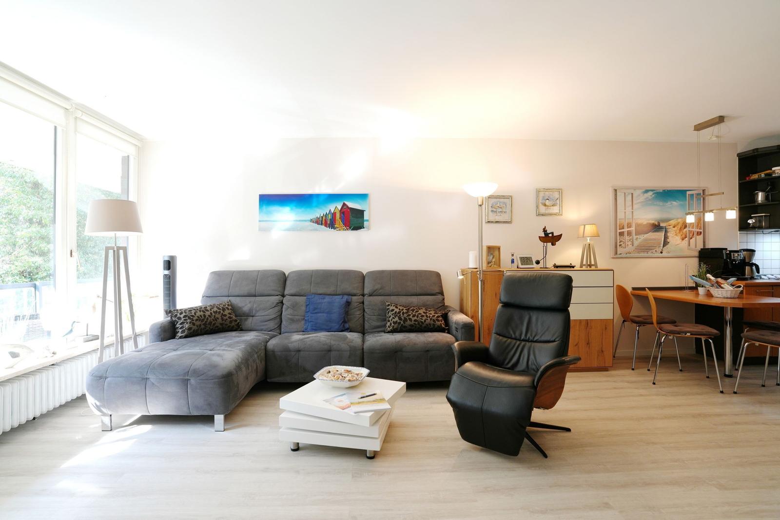 Living room with sofa, chair, and dining area. Large windows and wall art.