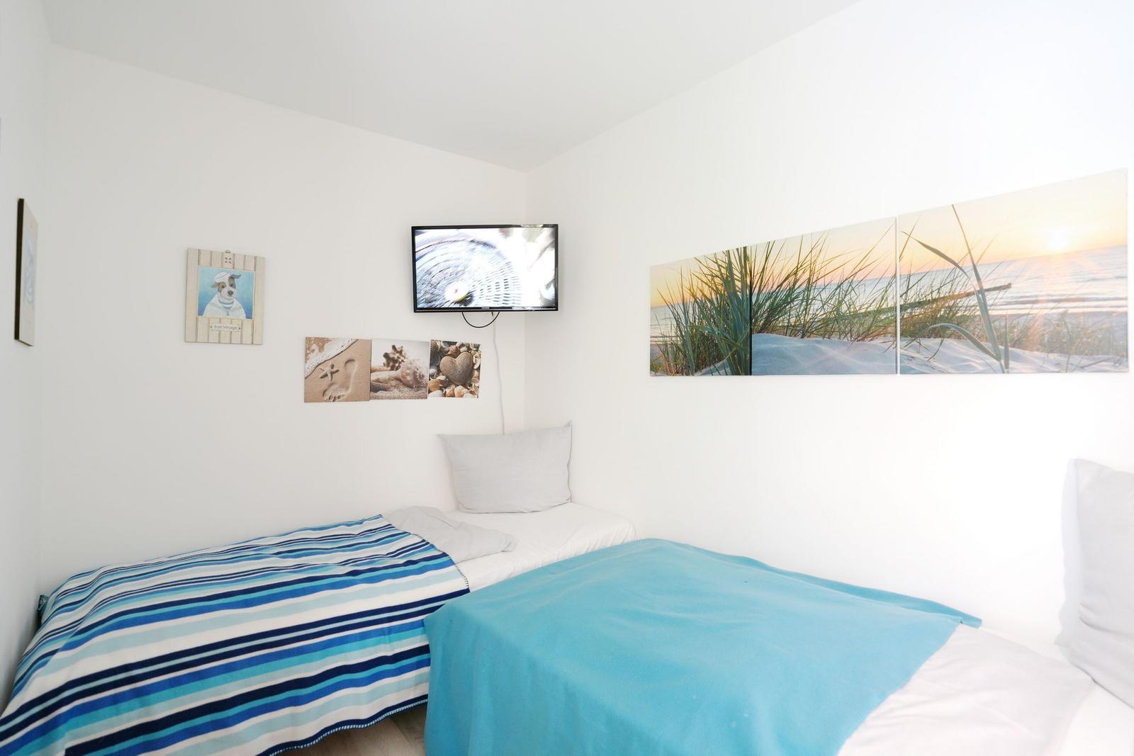Two beds with blue bedding, wall art with beach motif, and flat-screen TV.