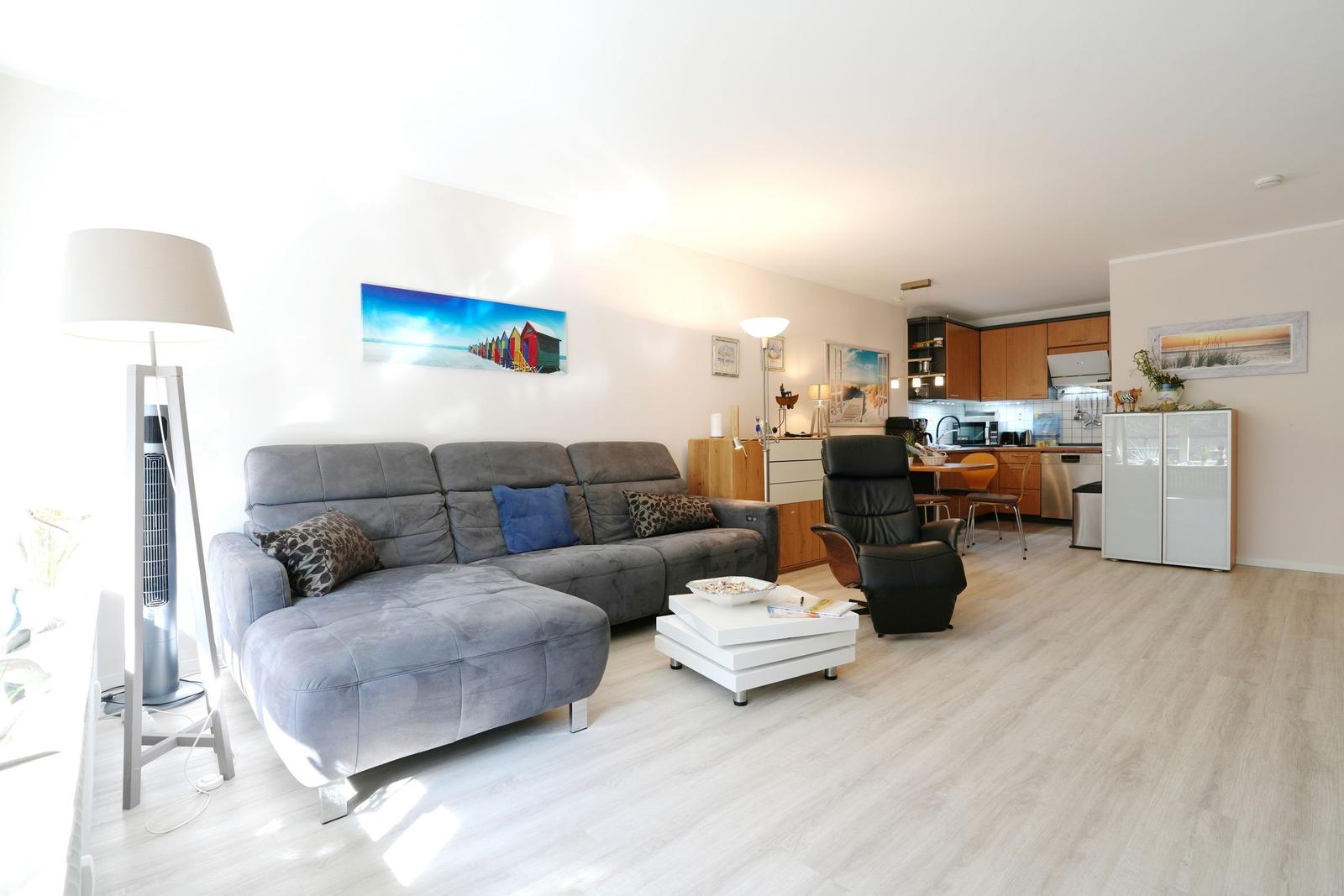 Living and kitchen area with sofa, armchair, and kitchen cabinets.