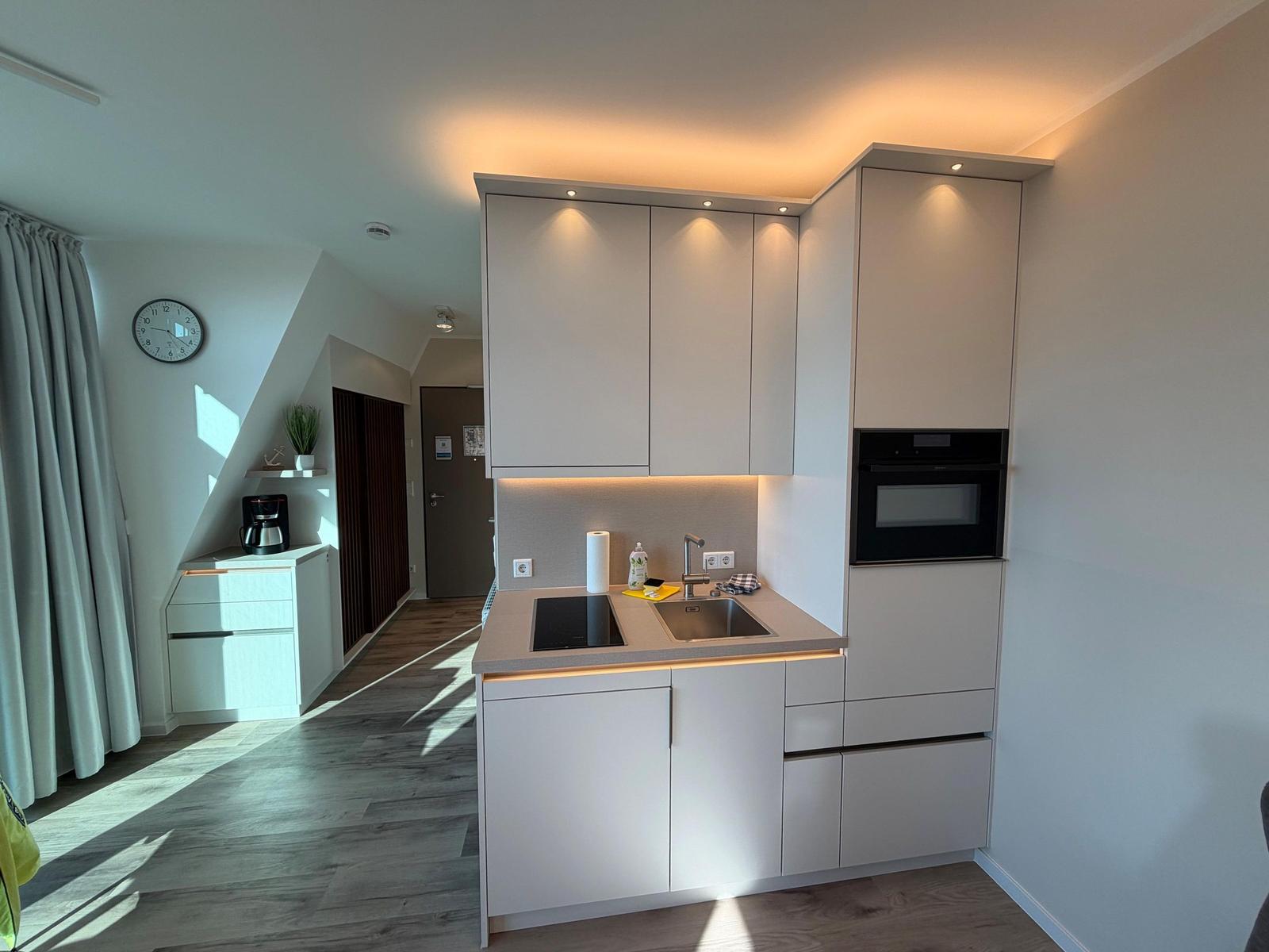 Moderne Küche mit eingebauter Spüle und Backofen. Helle Holzdielen und weiße Schränke.