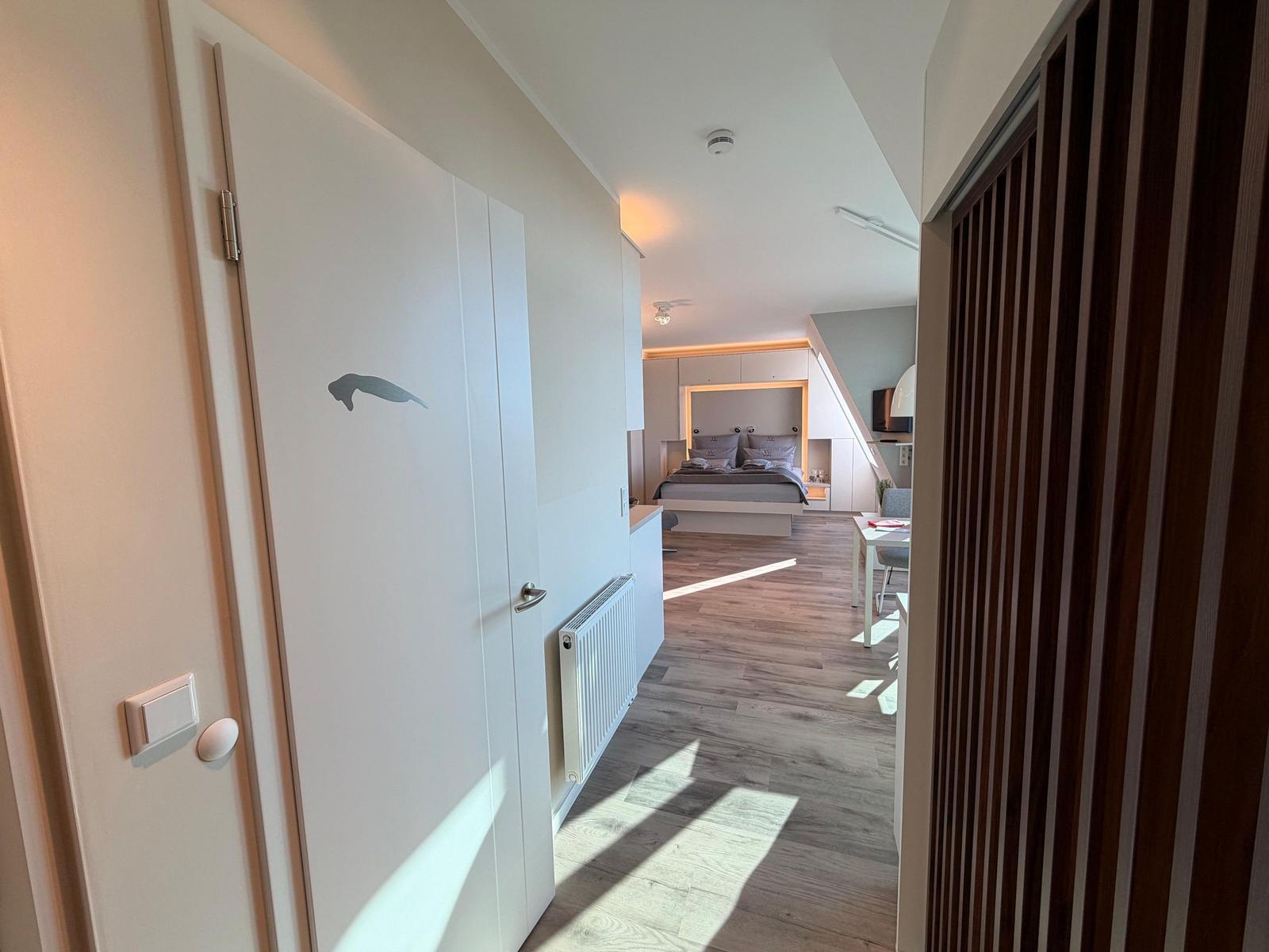 Schlafzimmer mit Bett, Tisch und Holzboden. Tür mit Delfinmotiv.