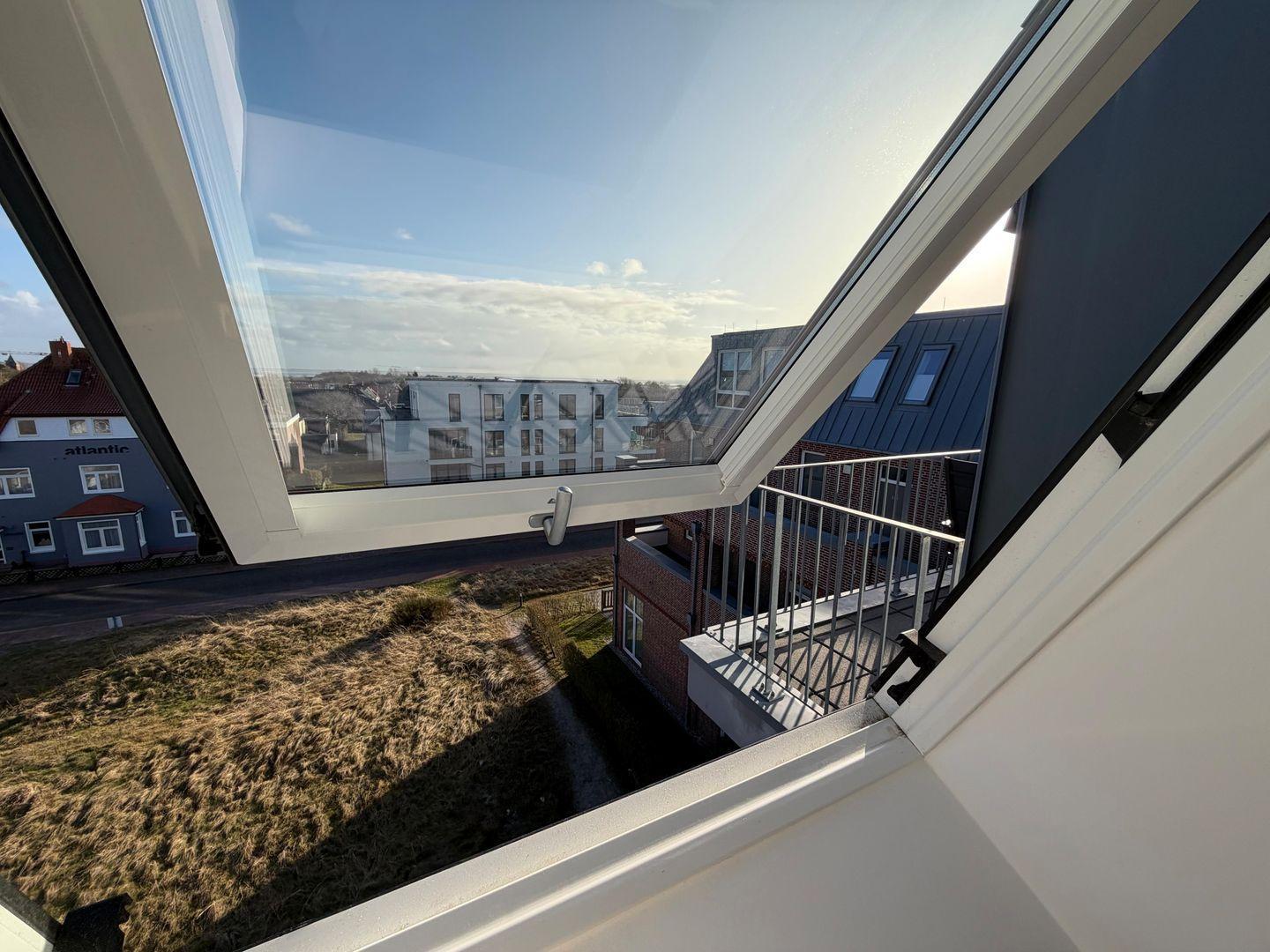 Durch das geöffnete Fenster ist die Aussicht auf Gebäude und Grünflächen zu sehen.