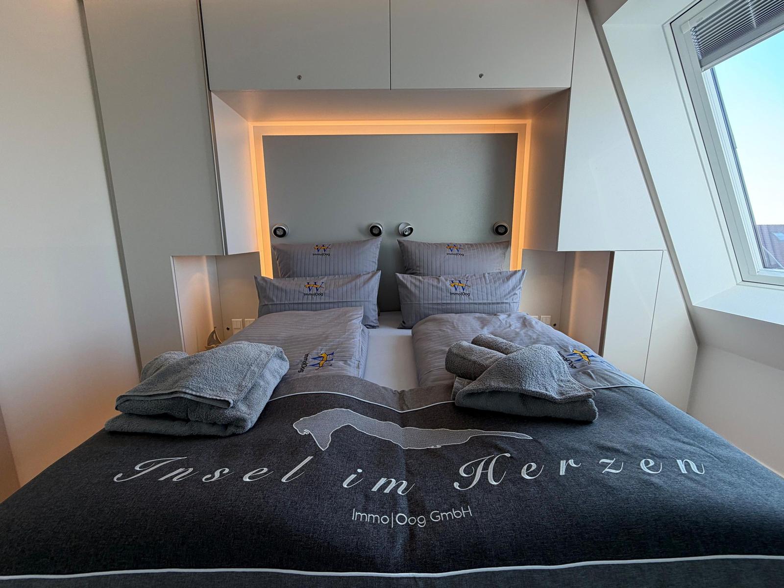 Doppelbett mit grauer Bettwäsche und Falttüchern unter Dachsatteldach