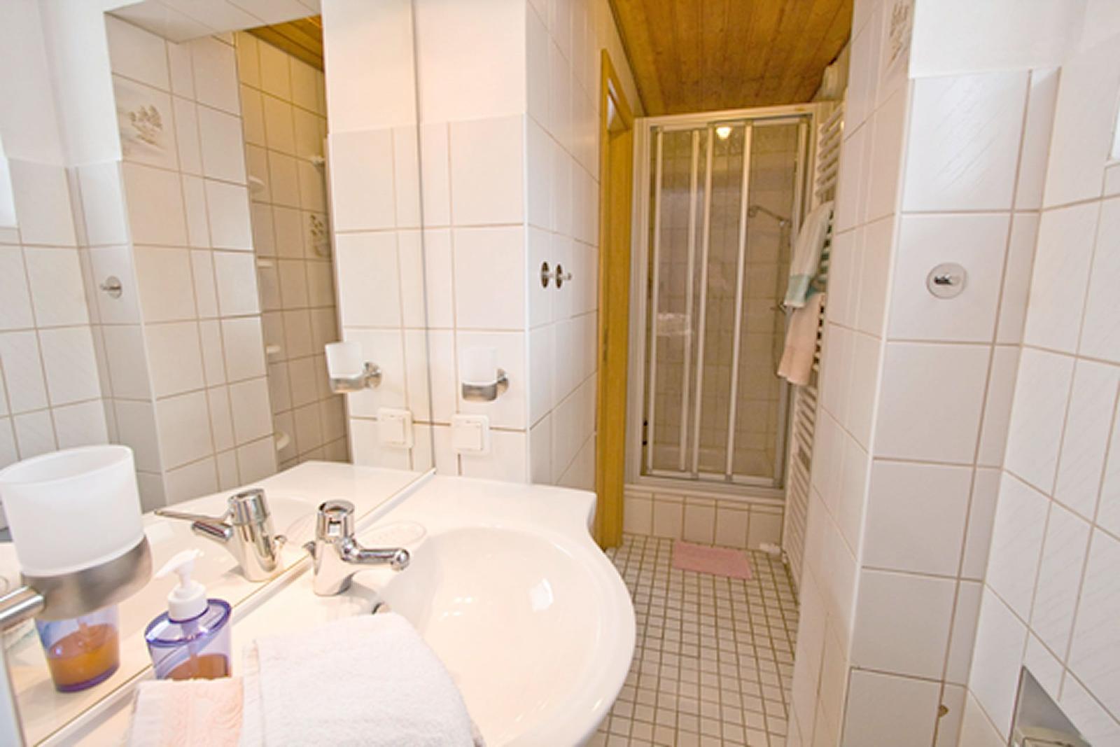 Bad mit Waschbecken, Spiegel und Dusche mit Glaswand.