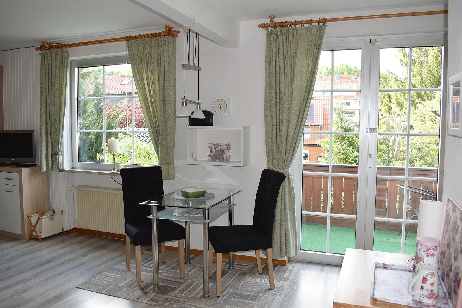 Esszimmer mit Tisch, zwei Stühlen, Fenstern und Balkontür.