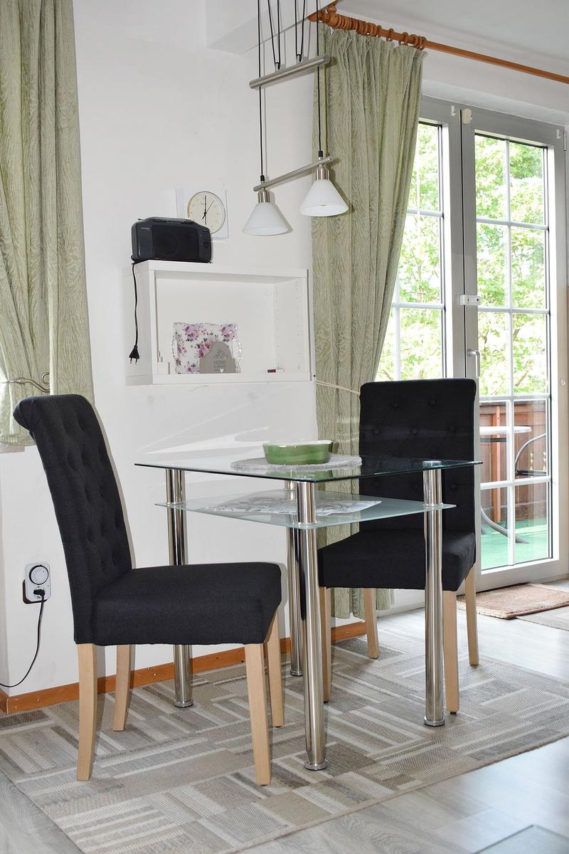 Esstisch mit zwei Stühlen, Glasplatte, vor Fenster mit Blick auf Balkon.