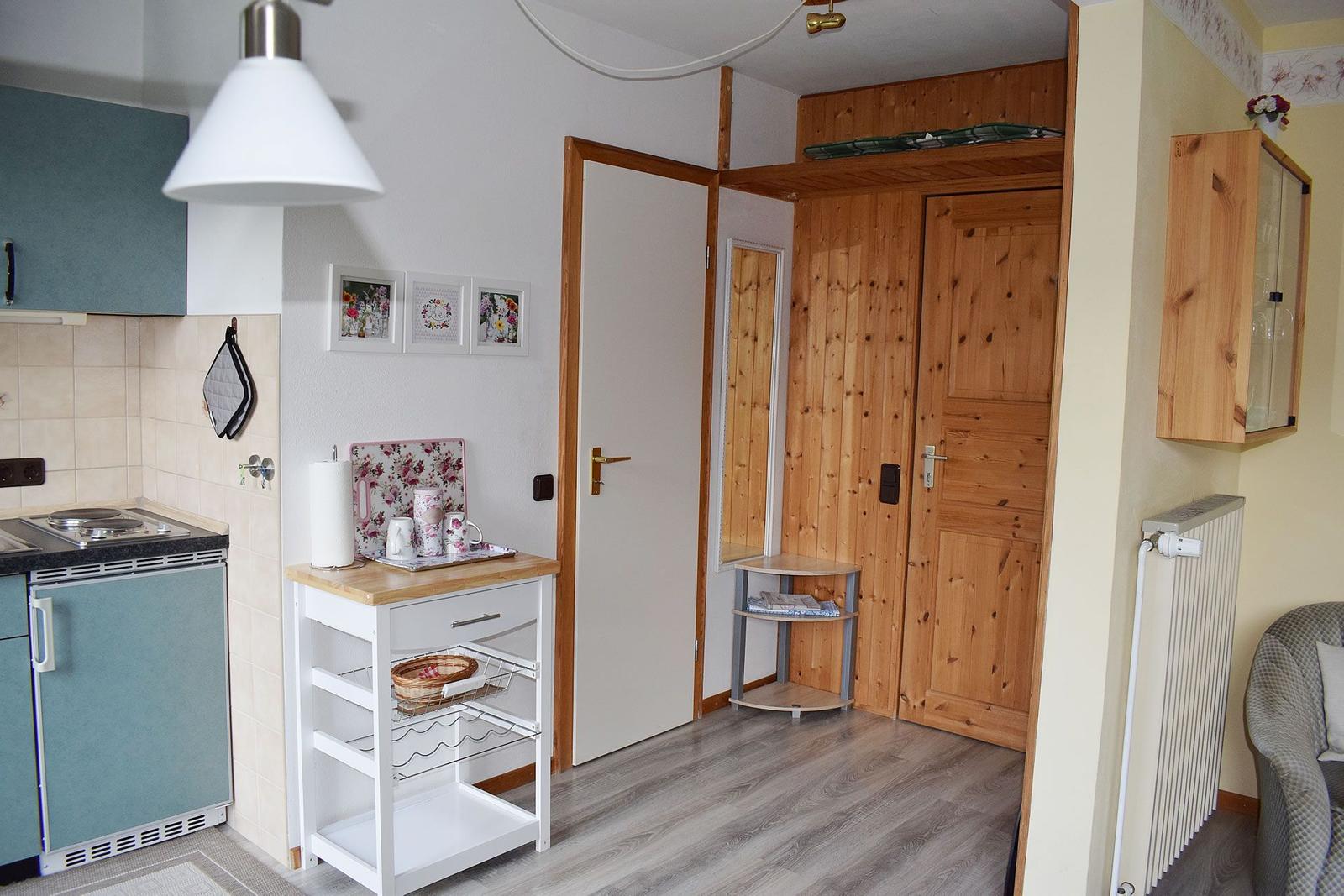 Küche mit Holzregal und Tür zum Schlafzimmer. Küchenzeile mit blauen Schränken.