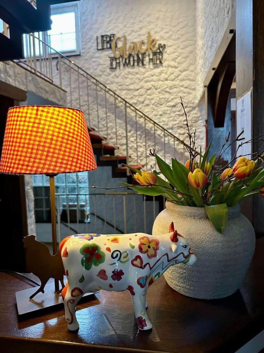 Tisch mit dekorativer Kuh, Blumen und Lampe vor Treppenhaus