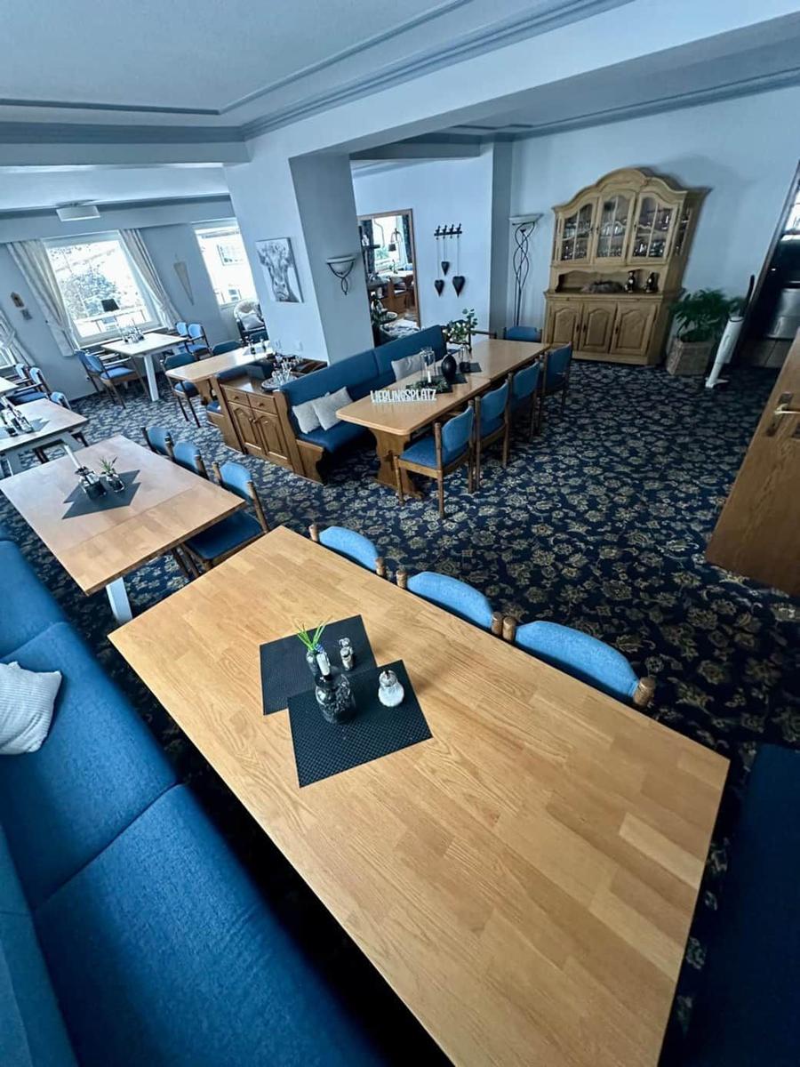 Großer Raum mit mehreren Tischen und blauen Sofas auf gemustertem Teppich.