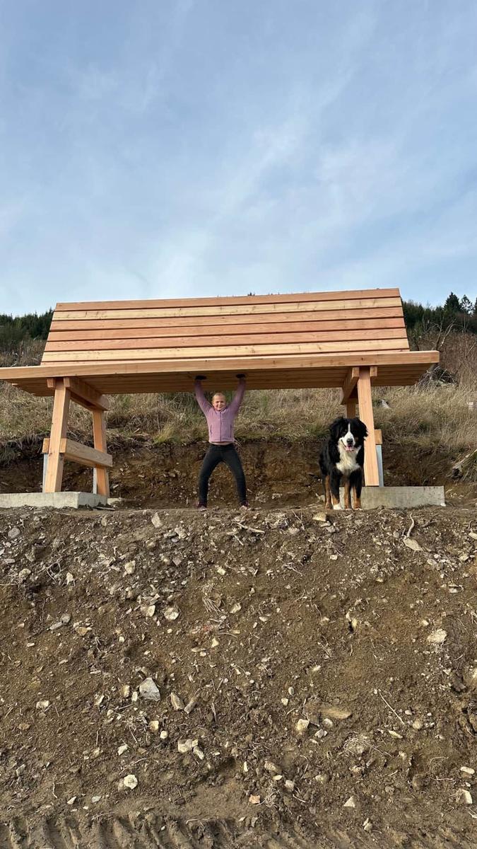 Eine Person und ein Bernhardiner stehen unter einem Holzüberdachung im Freien.