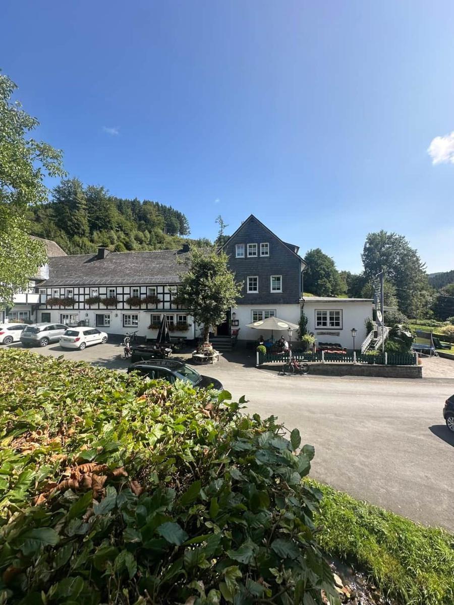 Traditionelles Haus mit Terrasse und Parkplatz vor grüner Landschaft.