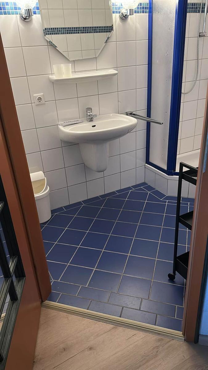 Badezimmer mit blau gefliestem Boden, Waschbecken und Dusche.