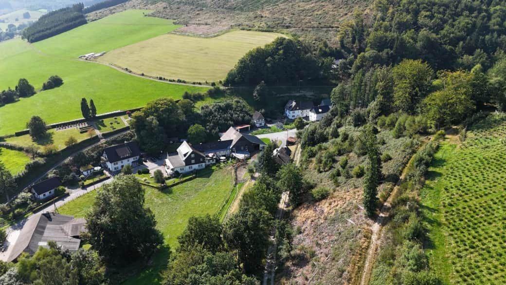 Aerial view of a rural property with houses, green fields, and dense forest.