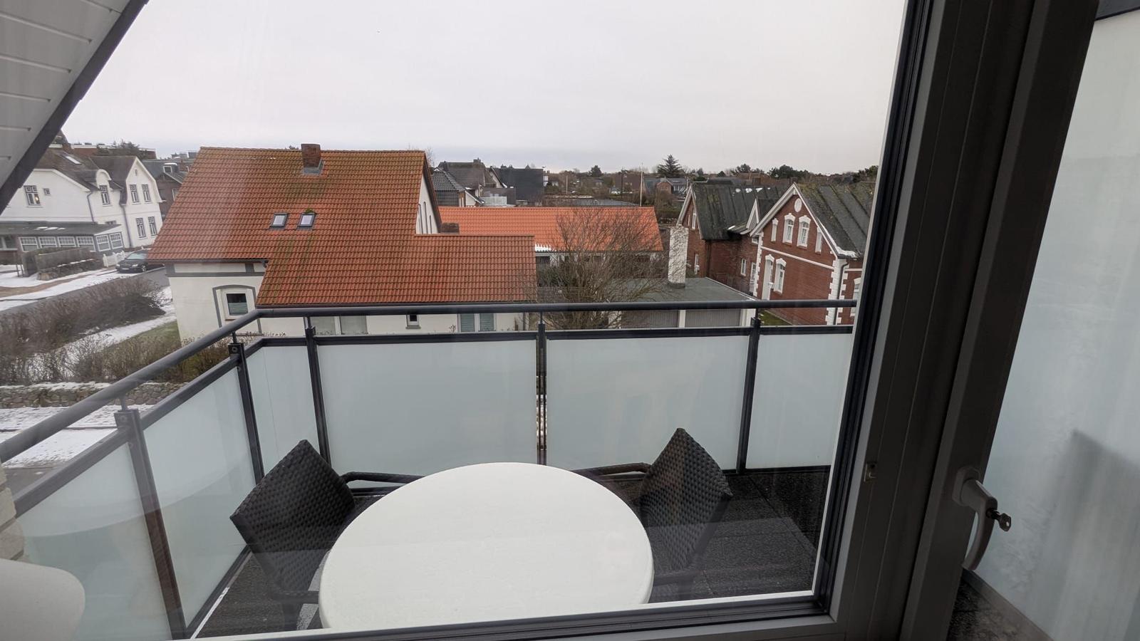Balcony with table and chairs overlooking rooftops and snowy ground.
