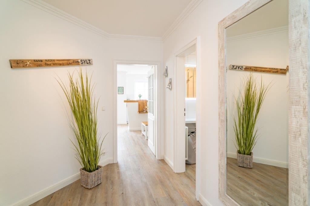 Flur mit Holzboden, großer Pflanze und Spiegel. Wanddekoration mit Schild.