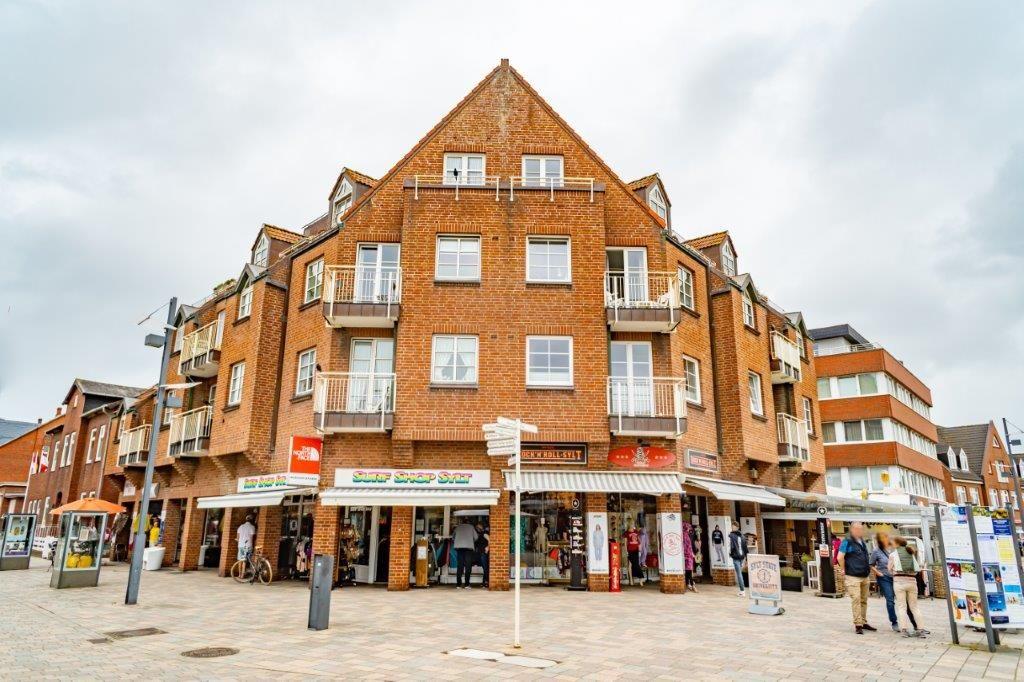 Zweistöckiges Backsteinhaus mit Geschäften im Erdgeschoss und Balkonen an den Fenstern.