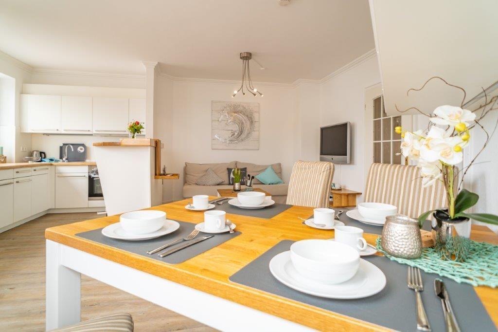 Essbereich mit Tisch, Stühlen und gedecktem Tisch. Küche und Wohnbereich im Hintergrund.