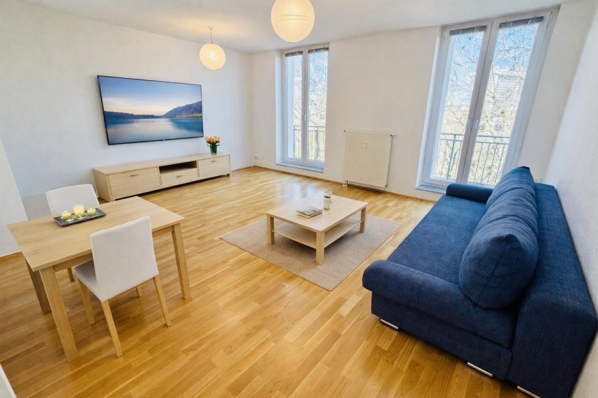 Wohnzimmer mit Sofa, Esstisch und Fernseher an der Wand.