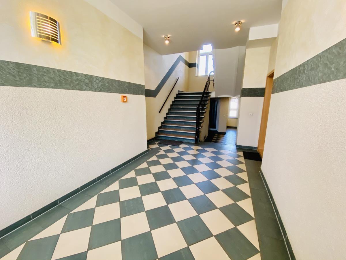 Halle mit schwarz-weißem Fliesenboden und Treppe nach oben.