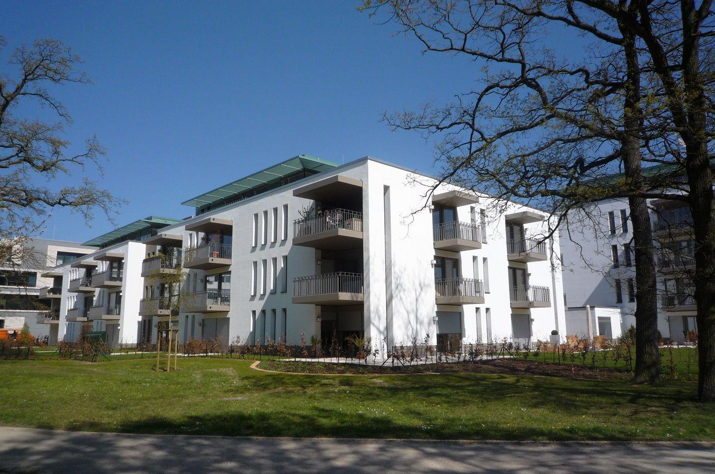 Moderne Wohnanlage mit Balkonen und grüner Umgebung unter blauem Himmel.