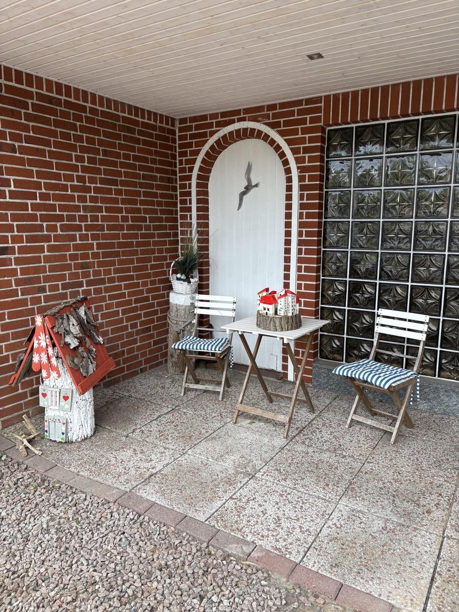 Terrasse mit Tisch, zwei Stühlen und dekorativen Häusern an der Backsteinwand.