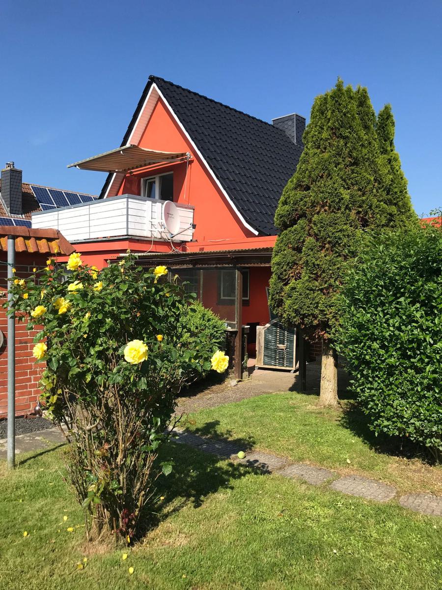 Rotes Haus mit Balkon, Solaranlage und Garten mit Rosen.