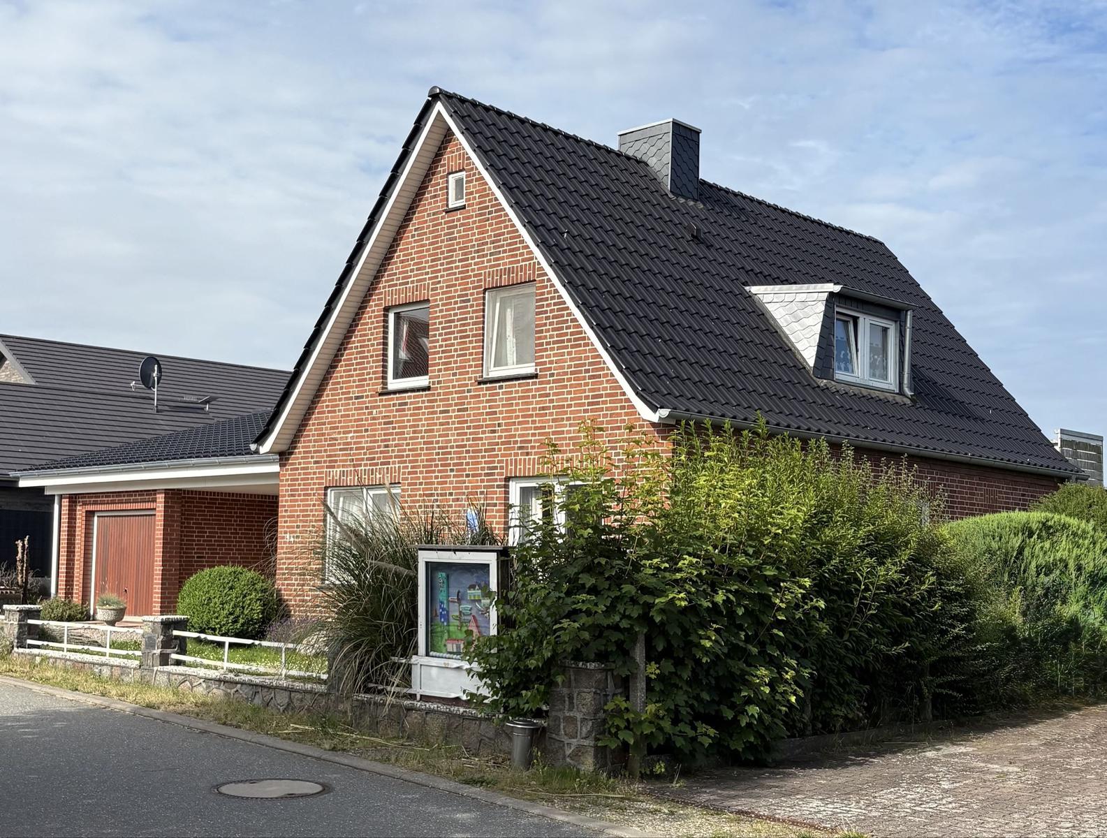 Rotes Backsteinhaus mit schwarzem Dach und grüner Hecke