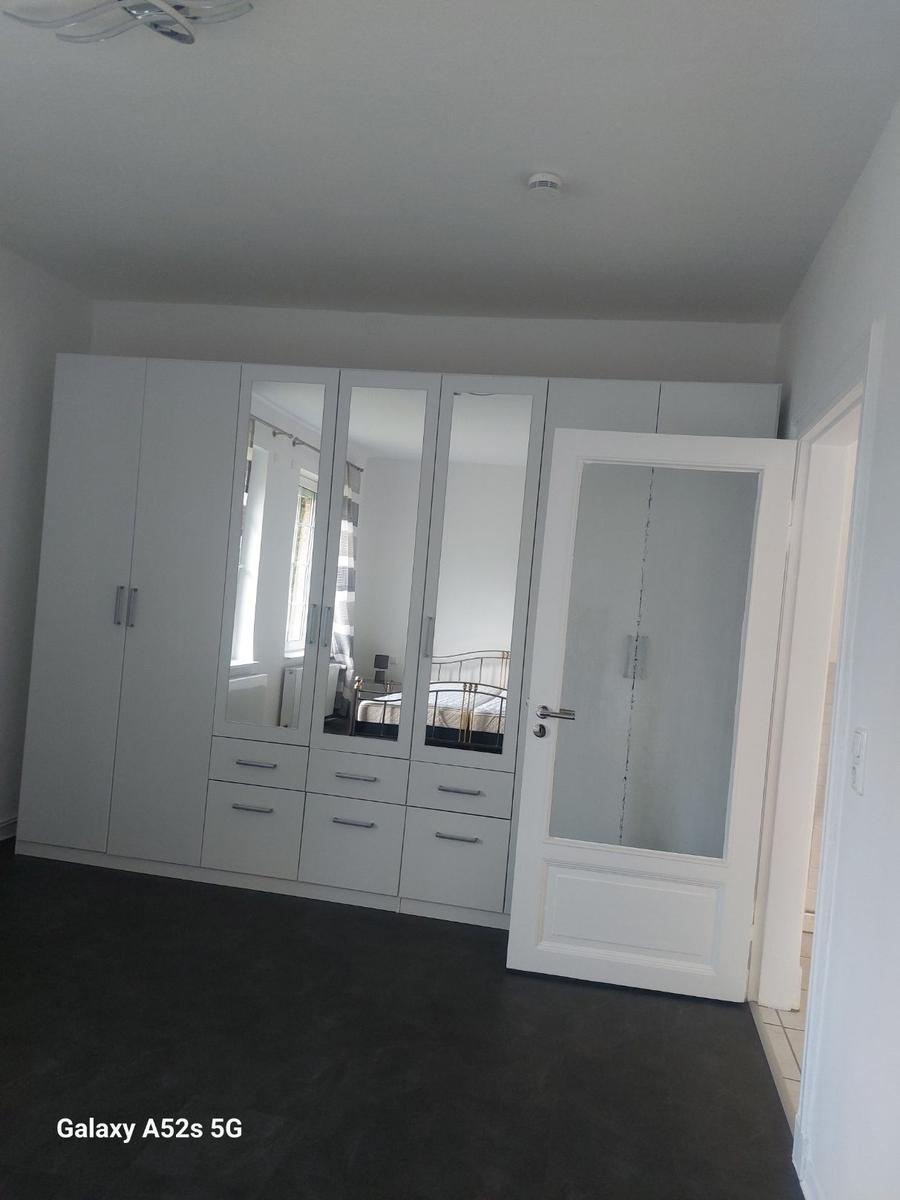 Schlafzimmer mit weißem Schrank und Spiegeltüren, dunkler Bodenfliese und Tür zum Anschlussraum.