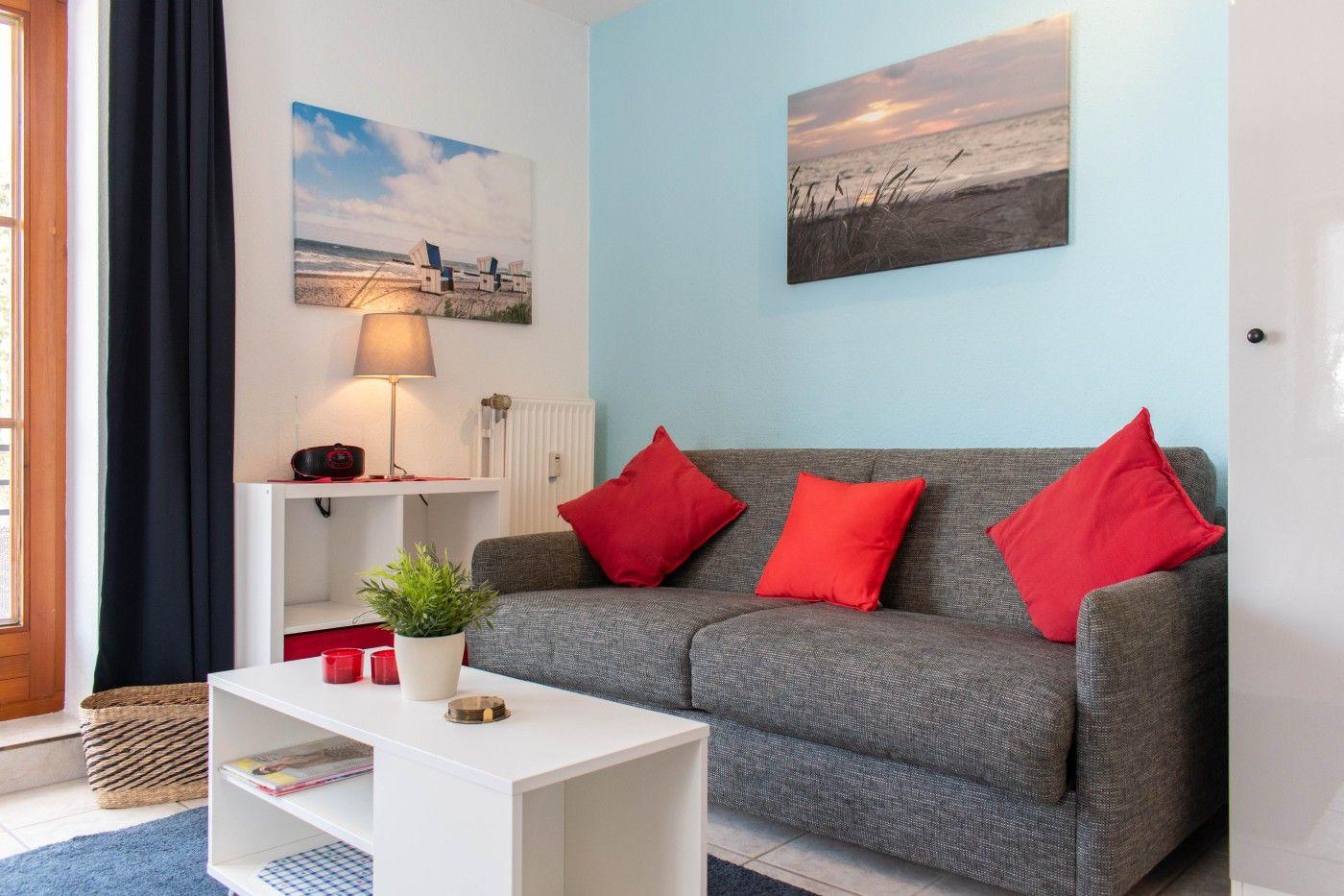 Ein Wohnzimmer mit grauem Sofa, roten Kissen und zwei Wandbildern an den Wänden.
