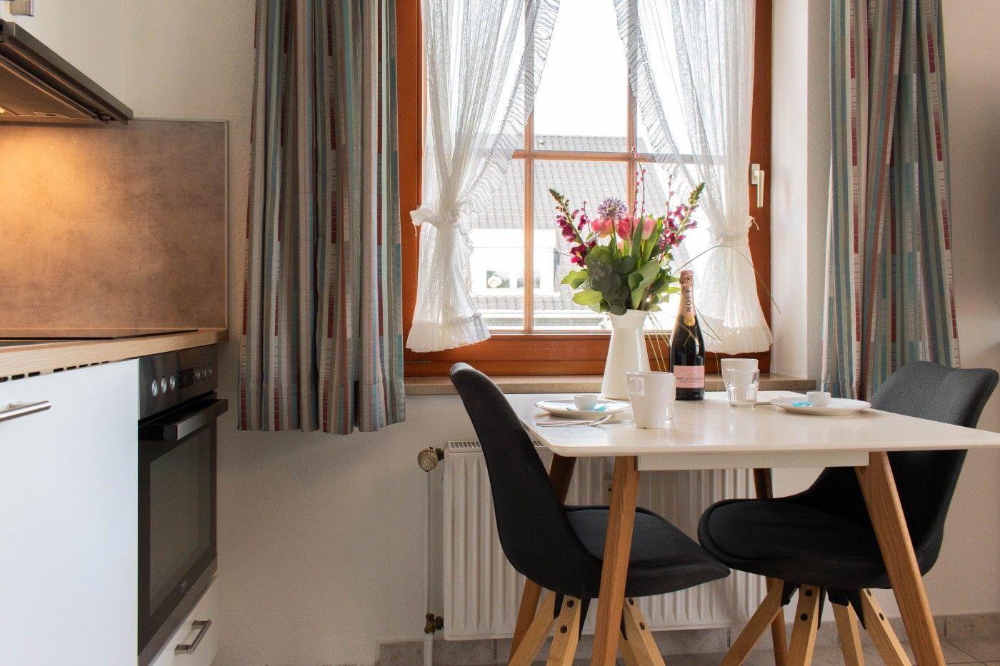 Essbereich mit Tisch, Stühlen und Fenster mit Blumen und Flasche.