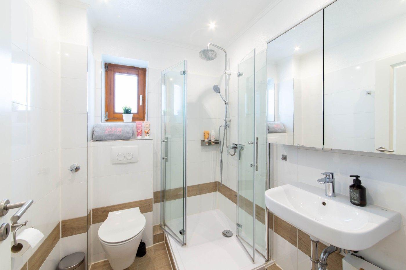 Badezimmer mit Dusche, Waschbecken und Toilette. Holzakzent an Wänden.
