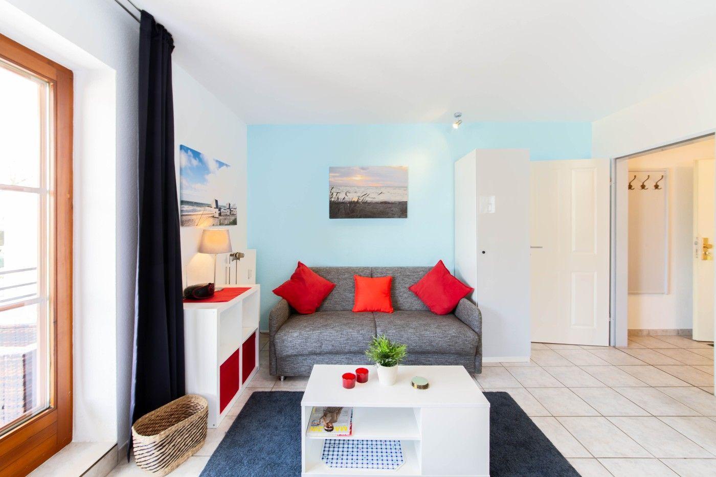 Wohnzimmer mit grauem Sofa, roten Kissen und weißem Couchtisch.
