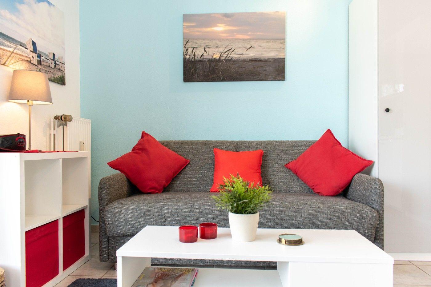 Ein Wohnzimmer mit grauem Sofa, roten Kissen und weißem Couchtisch.