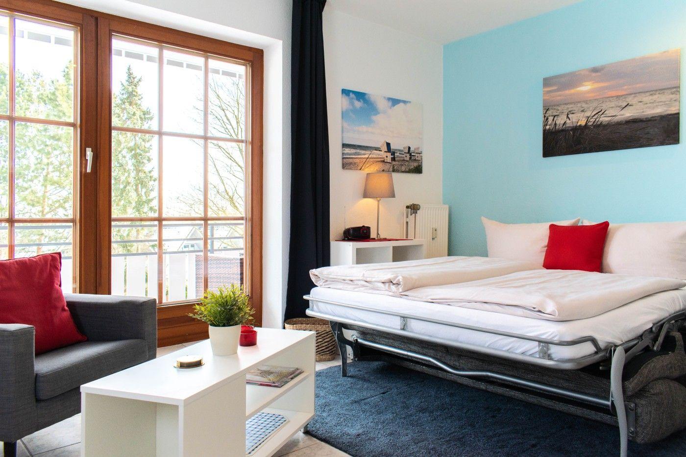 Schlafzimmer mit Bett, Sofa, Tisch und Fenster zur Terrasse.