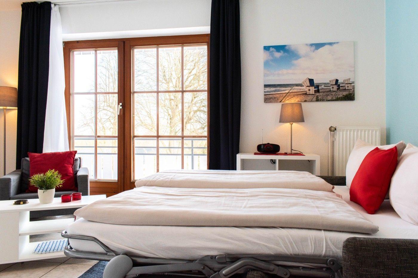 Schlafzimmer mit Doppelbett, Fenster und Sitzgelegenheit.