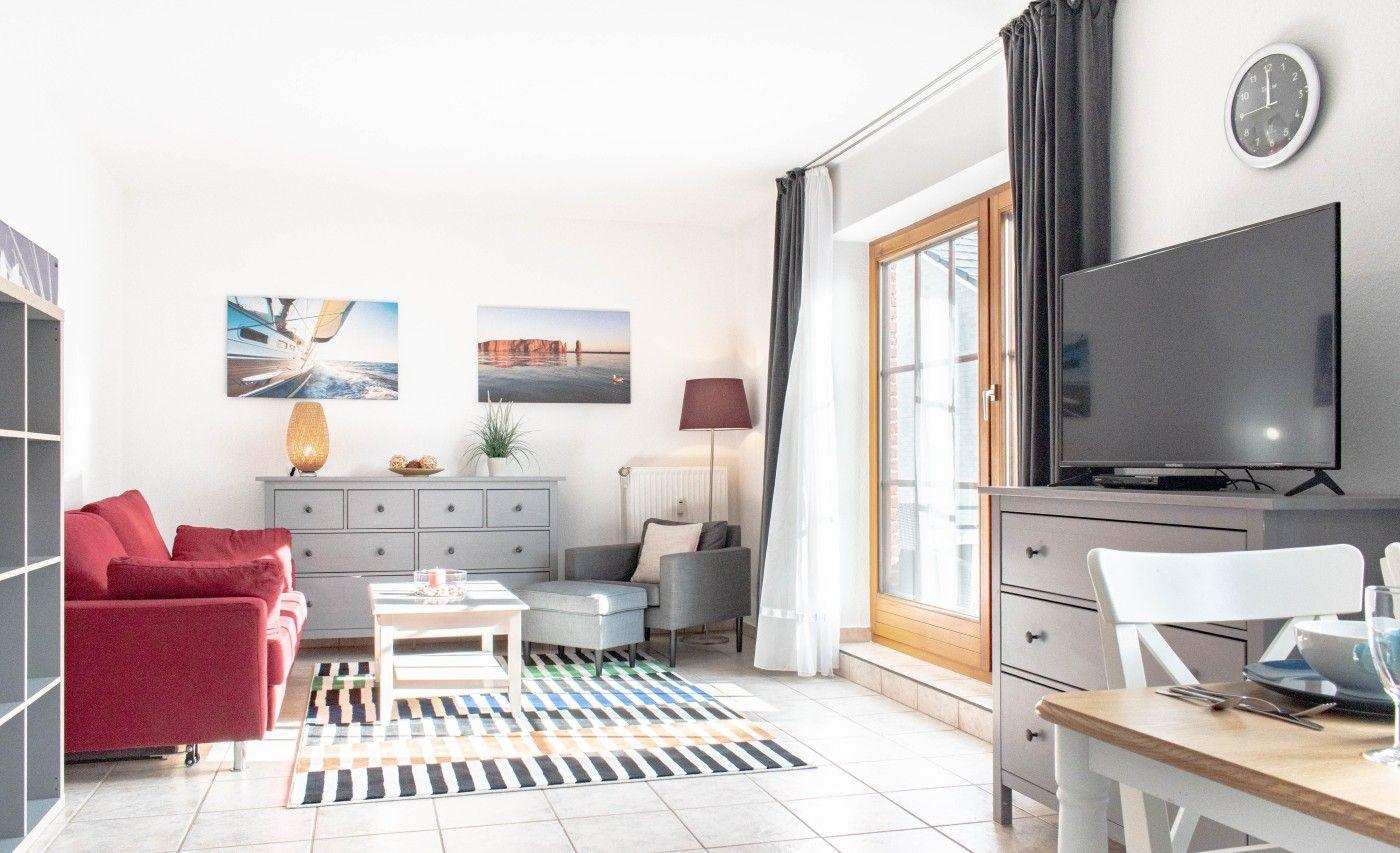 Wohnzimmer mit rotem Sofa, TV und Fenster. Wohnbereich mit Tisch und Stühlen.