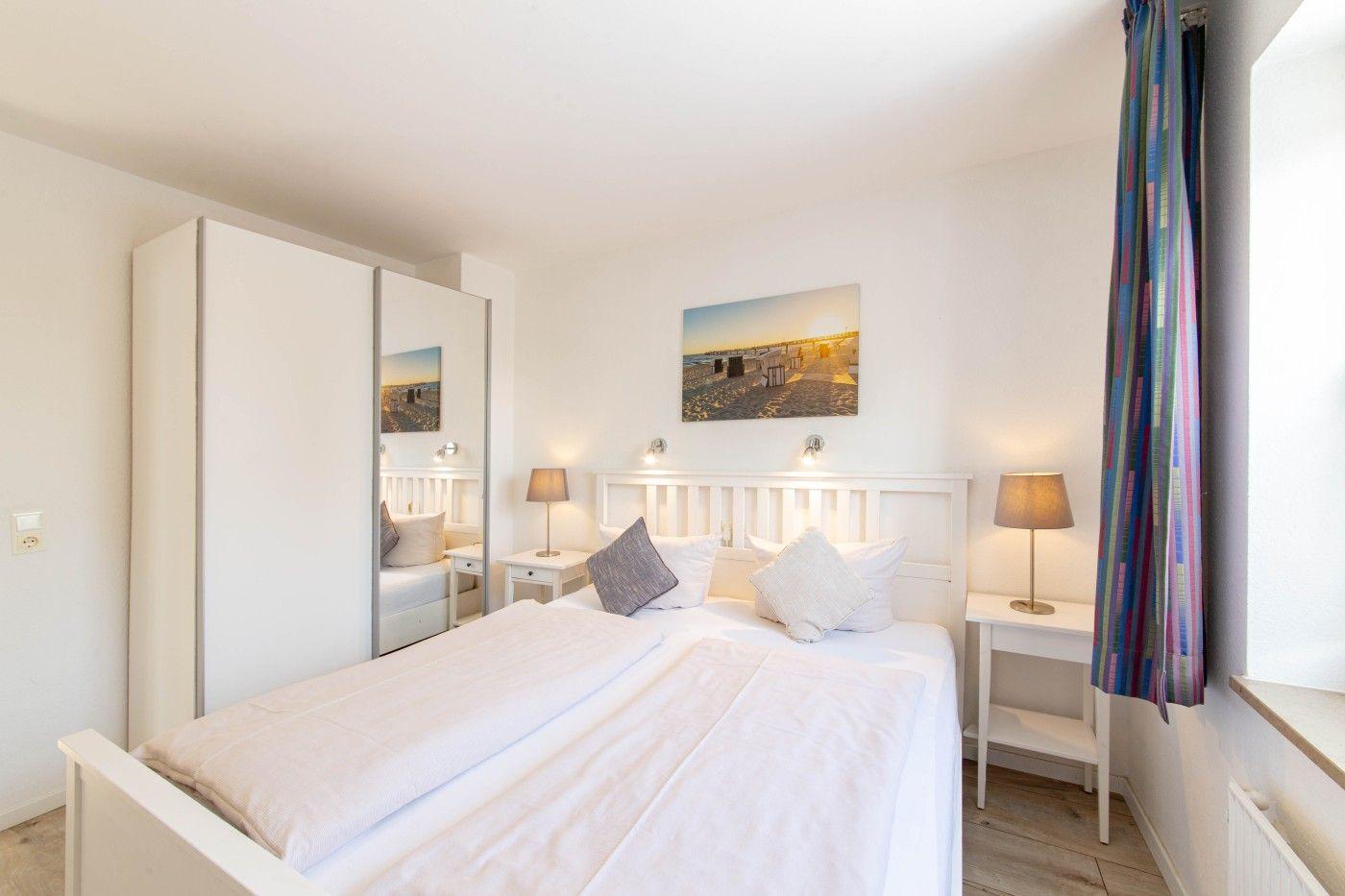 Schlafzimmer mit weißem Bett, zwei Nachttischen und Gardinen.