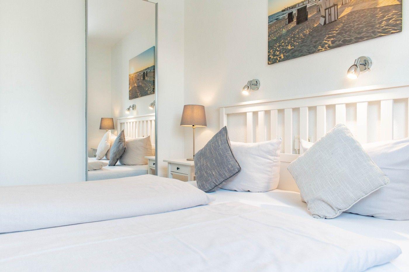 Schlafzimmer mit weißem Bett, Wandspiegel und Wandbild.