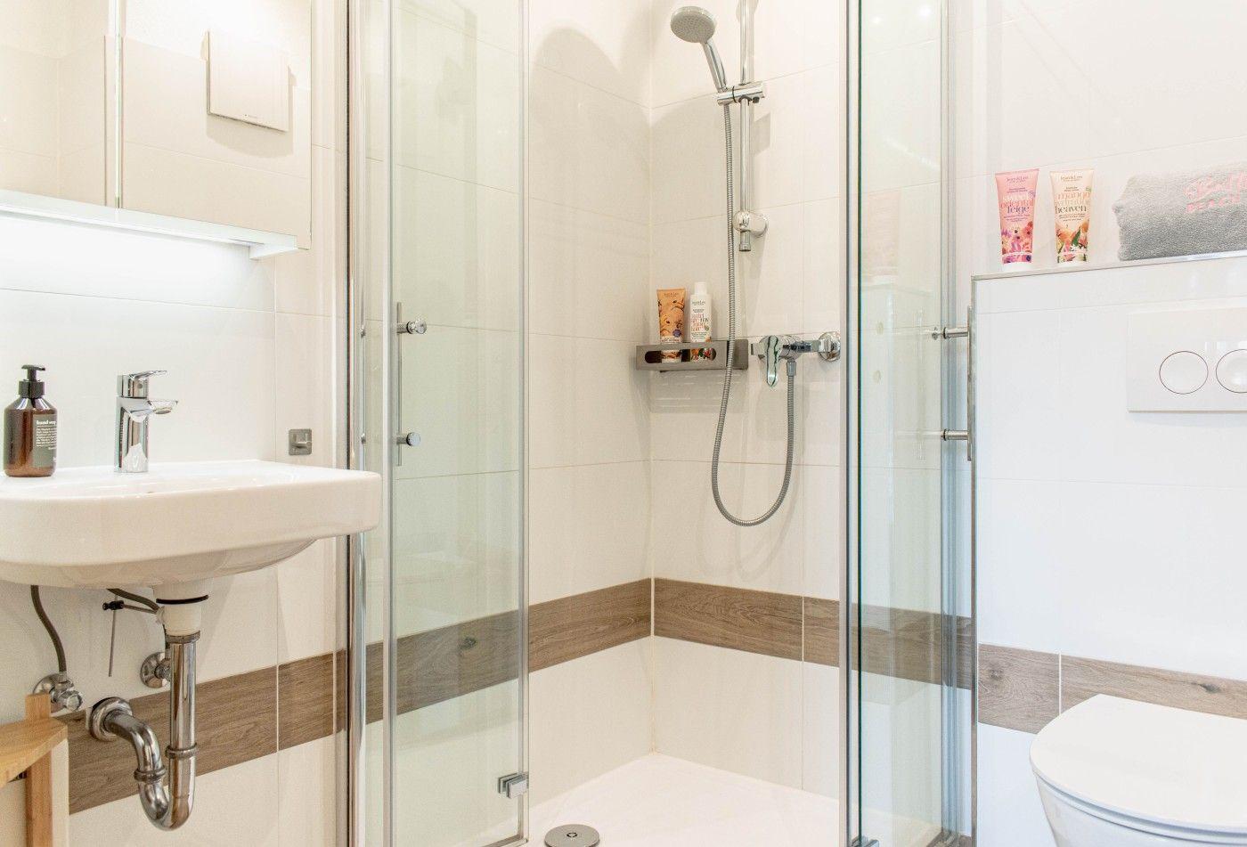 Badezimmer mit Dusche, Waschbecken und Toilette. Holzakzentstreifen an den Wänden.