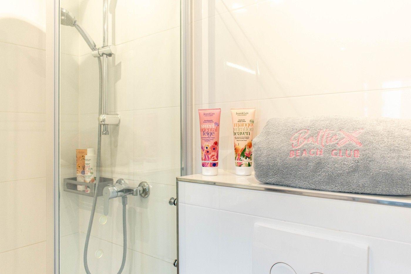 Dusche mit Duschbrause, Seife und Handtücher auf Waschbecken.