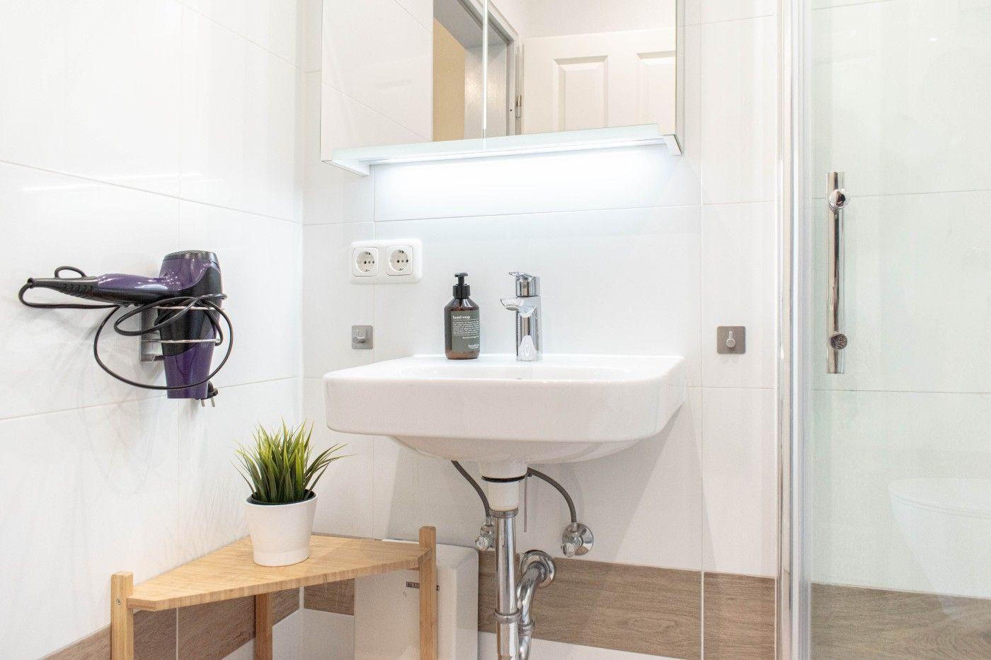 Badezimmer mit Waschbecken, Dusche und Haartrockner an der Wand.