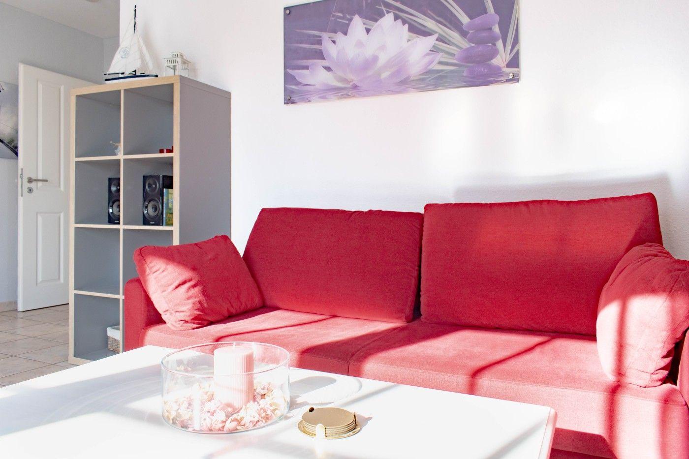 Rotes Sofa, weißer Tisch, Wandbild mit Lotus, Bücherregal und Tür im Hintergrund.