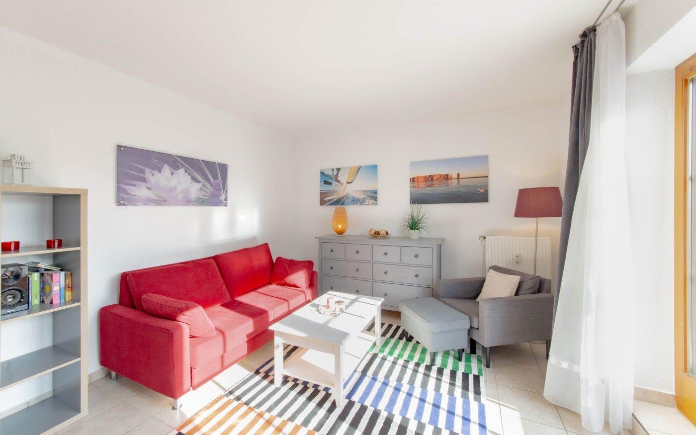 Wohnzimmer mit rotem Sofa, grauer Sitzgruppe und buntem Teppich.