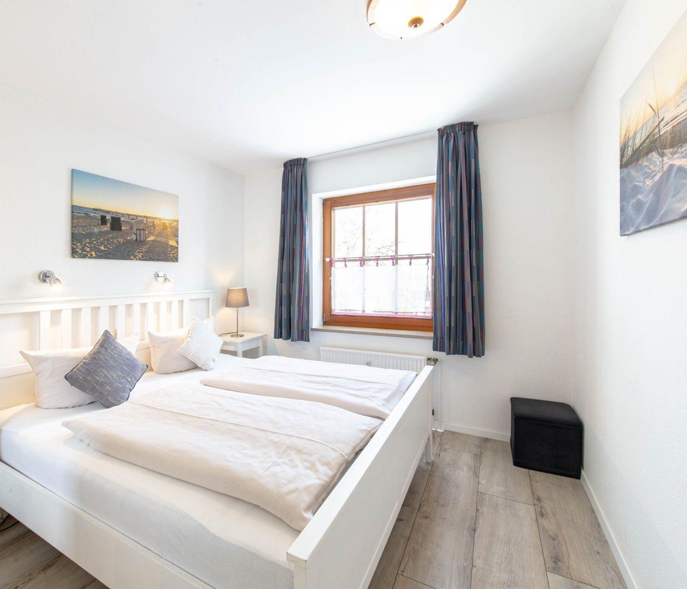 Schlafzimmer mit weißem Bett, Fenster und Wandbildern.