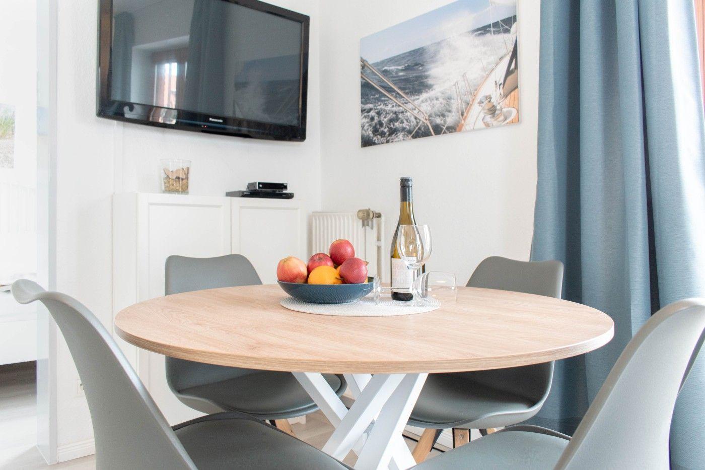 Runde Esstisch mit Stühlen, Fernseher und Wandbild.