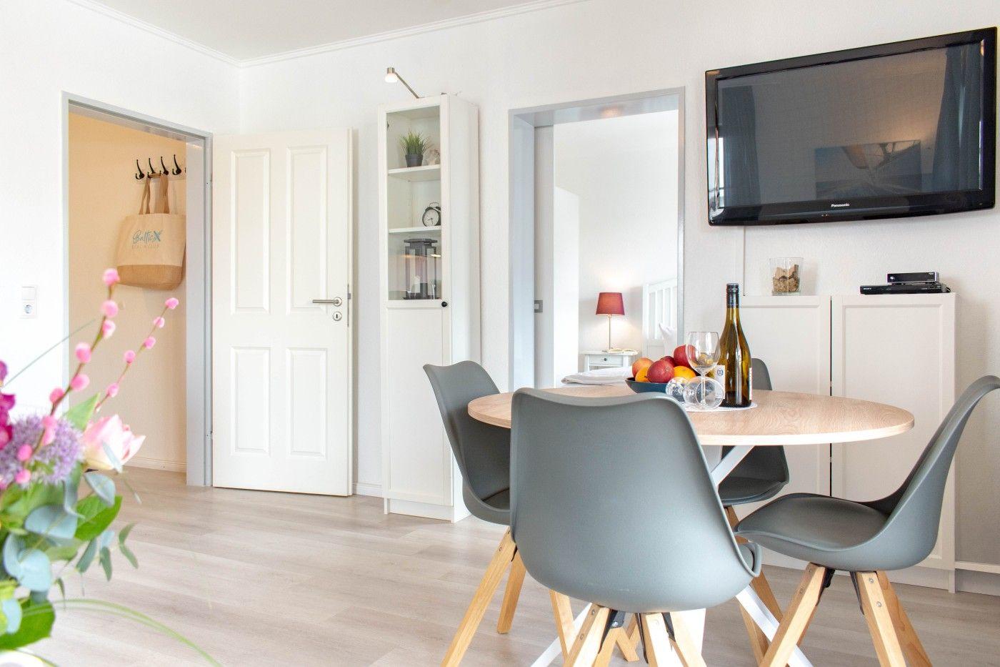 Essbereich mit runder Tisch, grauen Stühlen und Fernseher an der Wand.