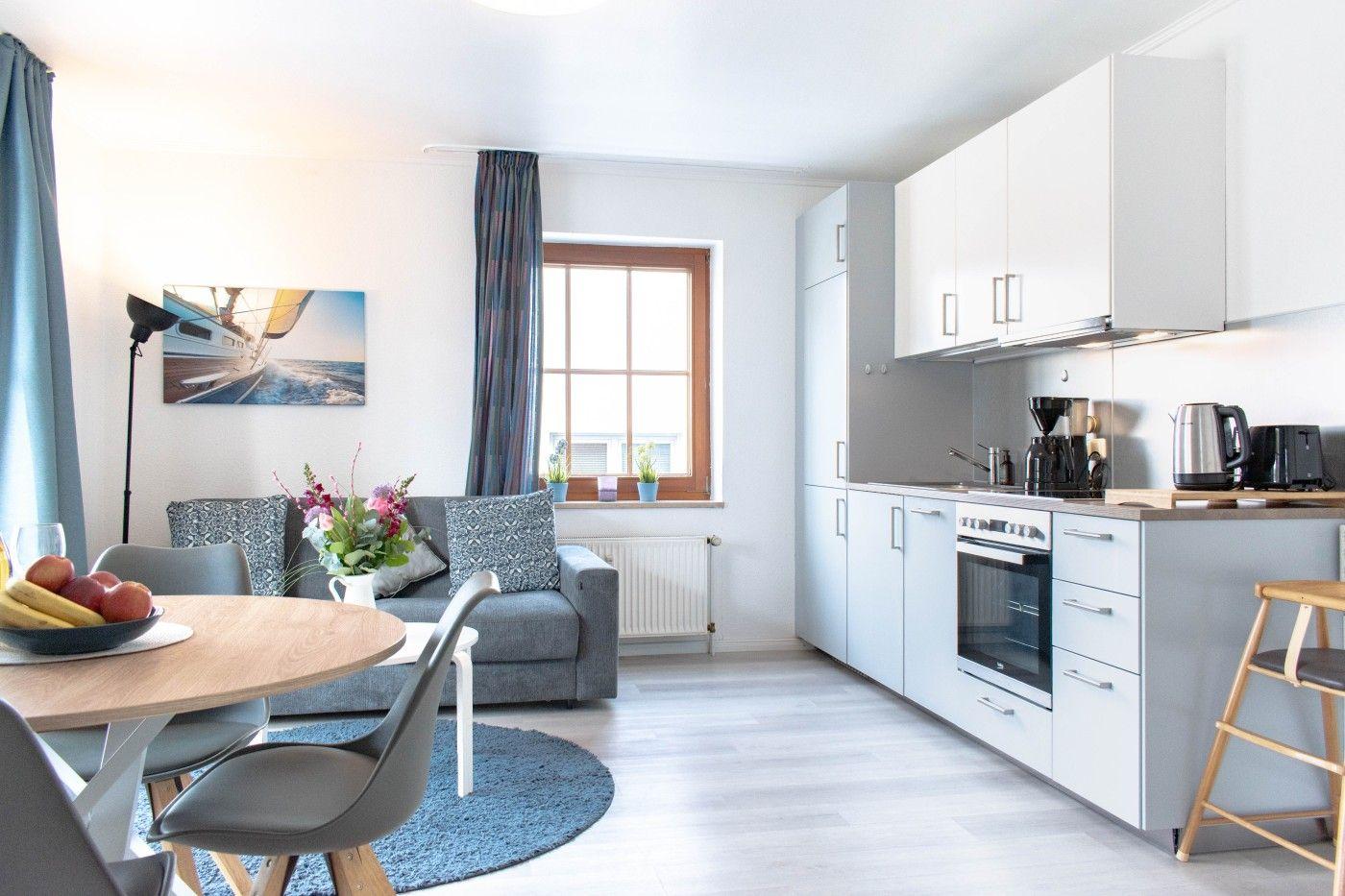 Wohnküche mit grauem Sofa, Essplatz und Küchenzeile.