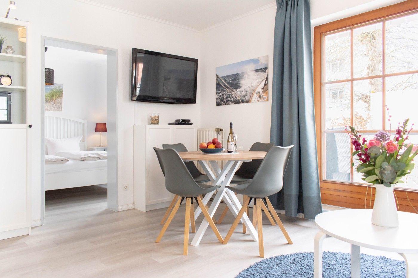 Wohnraum mit Esstisch, TV und Blick auf Balkon. Schlafzimmer im Hintergrund.