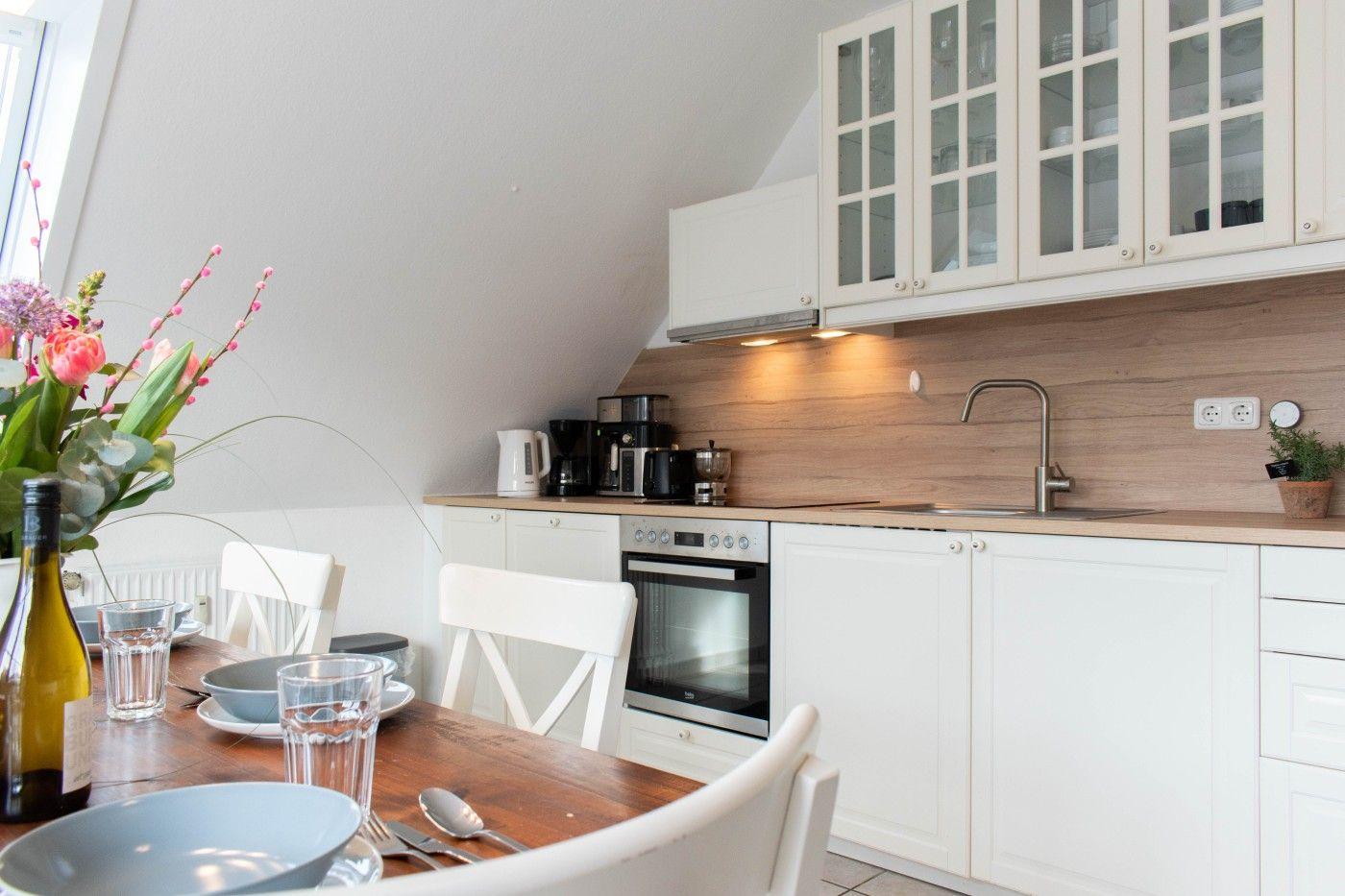 Küche mit Esstisch, weißen Schränken und Holzrückwand.